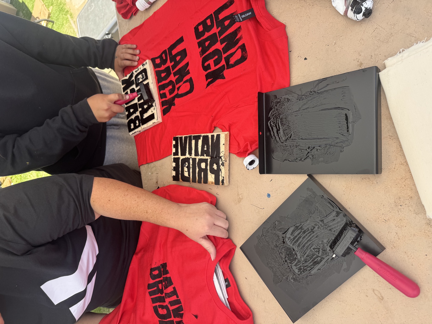 Young people printing LAND BACK designs on red T-shirts.
